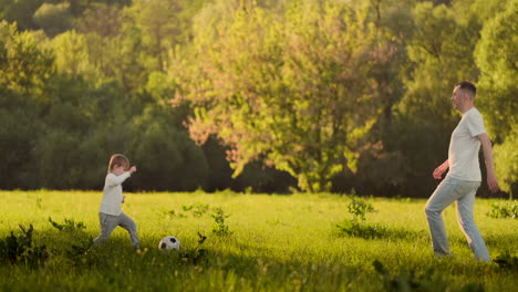 A-young-father-in-a-white-t-shirt-with-two-sons-playing-football-on-the-grass-at-sunset-in-the-sun-in-slow-motion